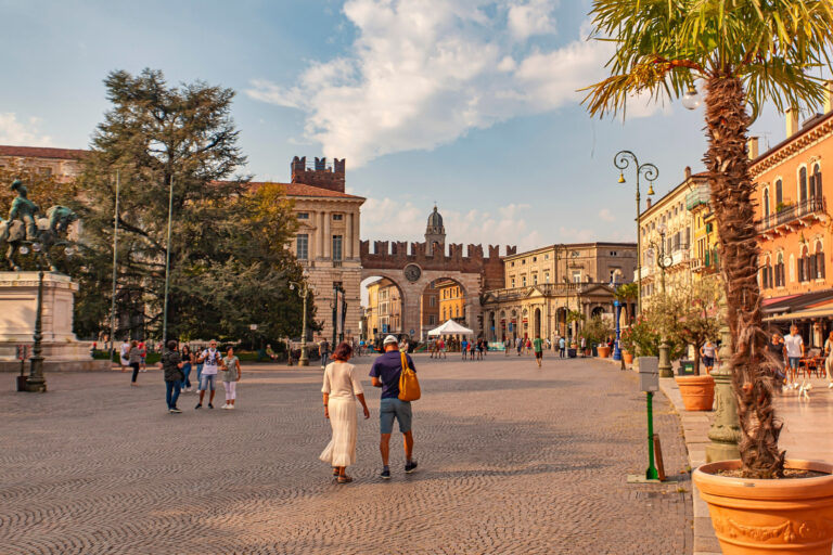 Verona, Italy 1 January 2025: Tourists walking in piazza bra square in verona, italy, with portoni della bra city gate in background on sunny summer day