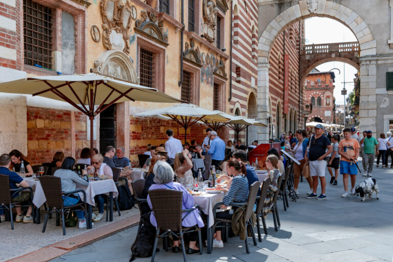 ITALY, VERONA, 16, MAY, 2024: People have lunch on the summer terrace of Caffe Dante restaurant in Piazza dei Signori (with the Loggia del Consiglio and Palazzo degli Scaligeri behind), Verona, Italy
